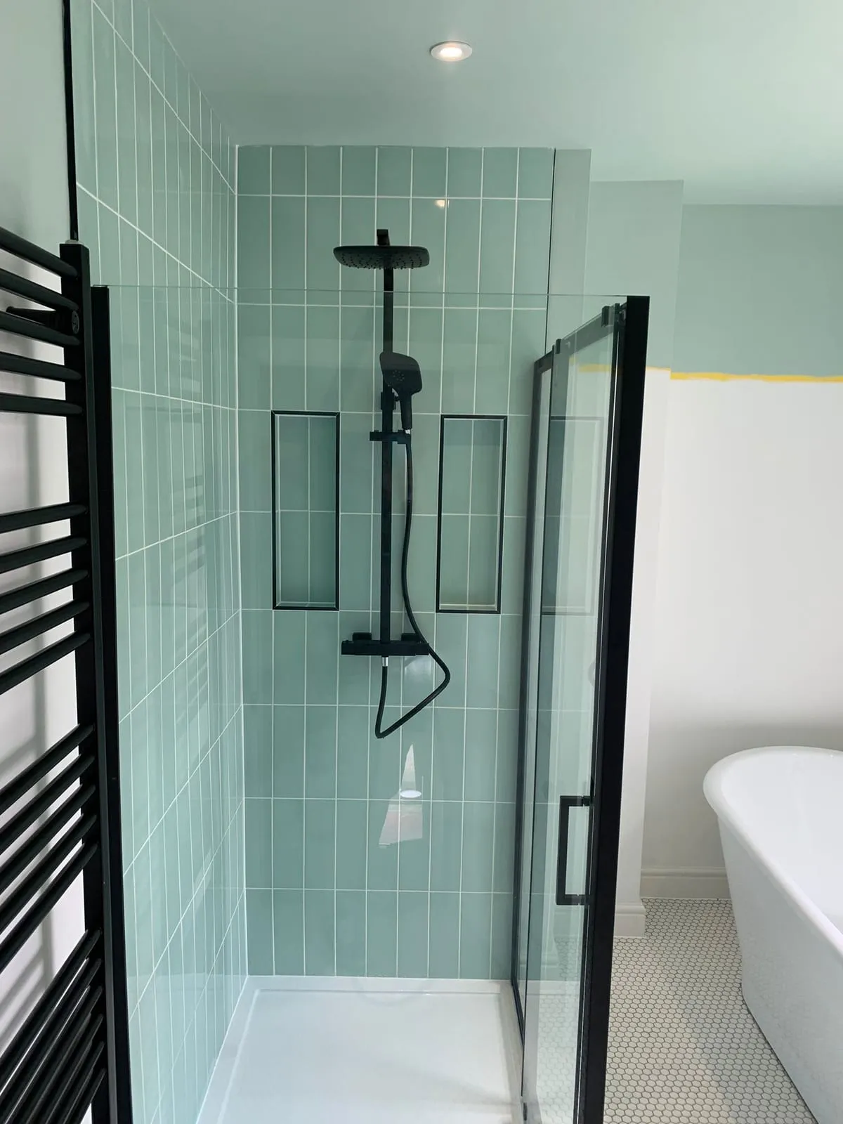 A black-framed shower enclosure with a black shower set against pale green tiling