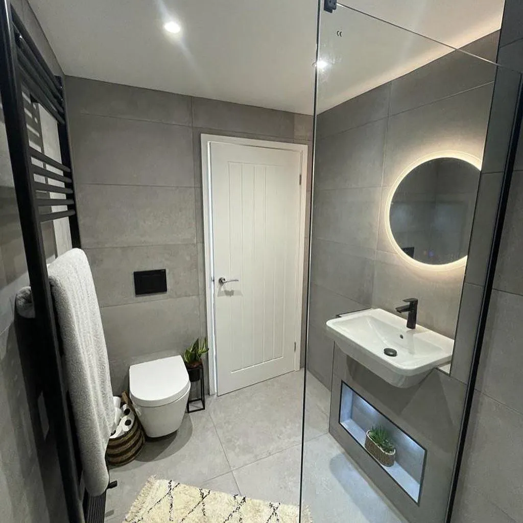 A grey-tiled bathroom with a back-to-wall toilet, a wall-hung basin and a round backlit mirror
