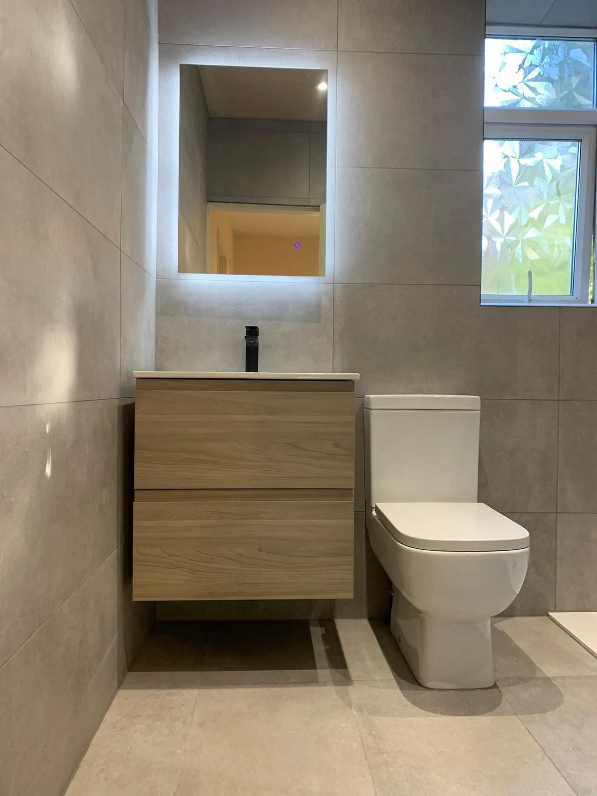 A timber vanity unit and basin beside a close-coupled toilet in a tiled bathroom