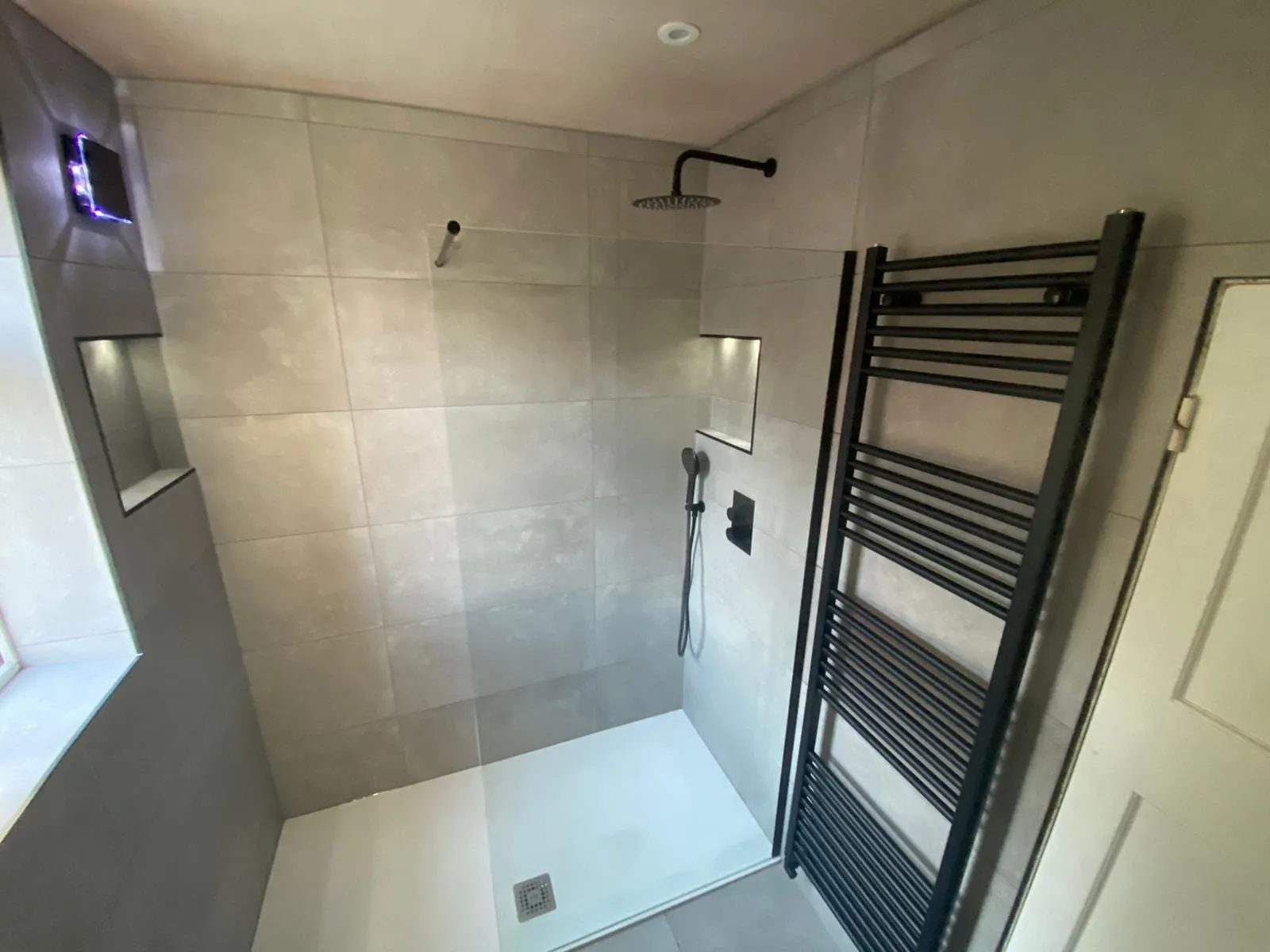 A grey-tiled walk-in shower with a black shower set and a matching black towel rail