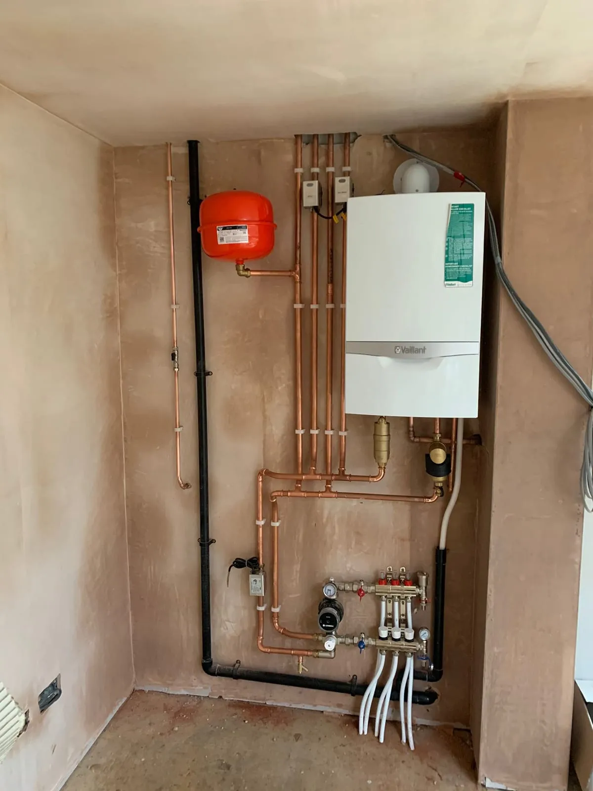 A boiler mounted on a board with a red expansion vessel and copper pipework run in alongside