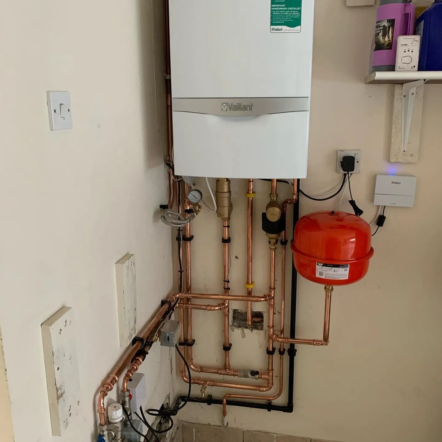 A boiler with a red expansion vessel and copper pipework mounted beside it