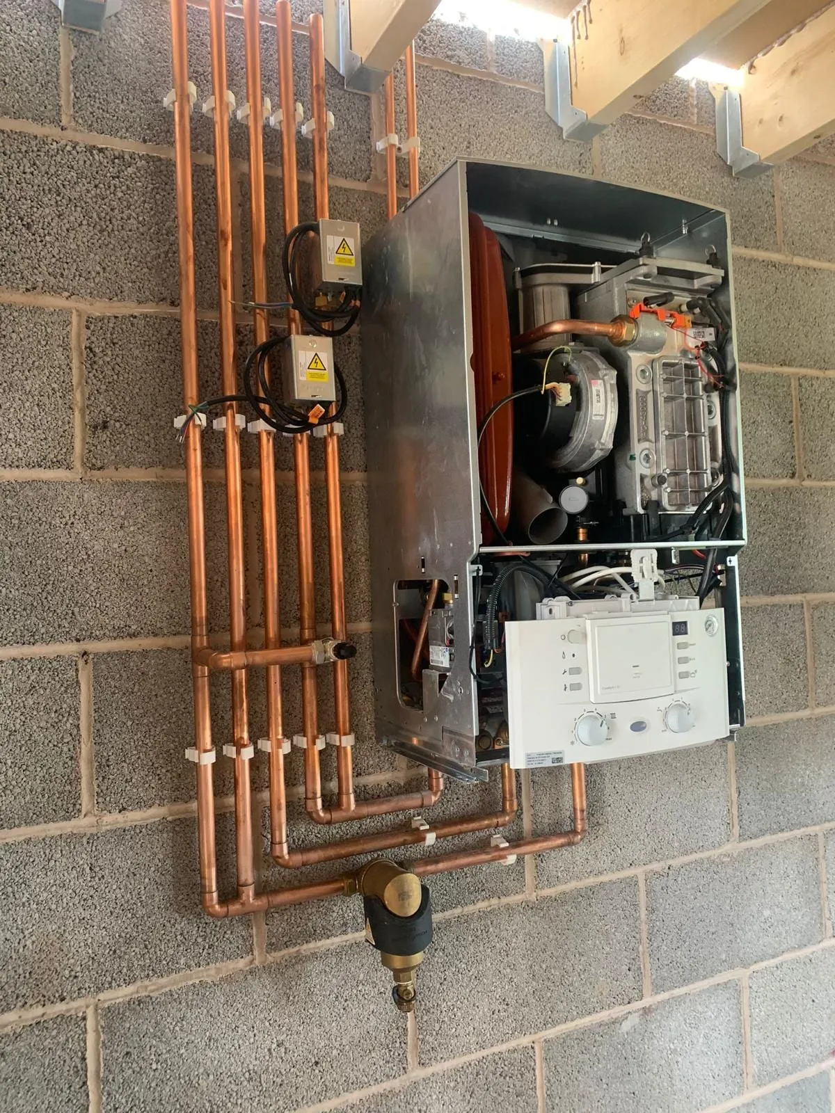 A boiler opened up for servicing on a brick wall, with copper pipework and controls exposed
