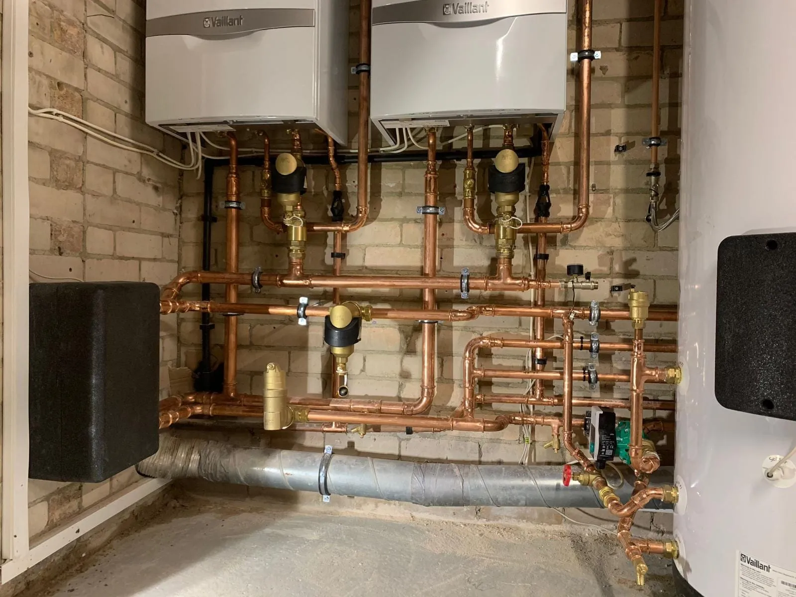 Two wall-hung boilers linked by copper and steel pipework in a commercial plant space
