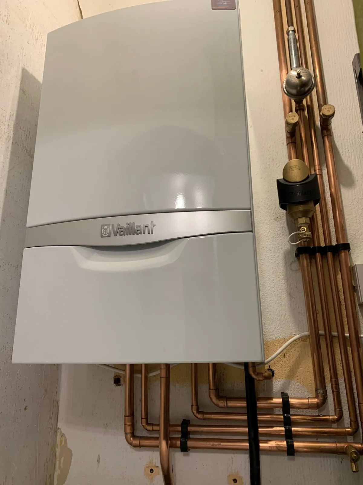 A wall-hung gas boiler with copper pipework and valves run up the wall next to it