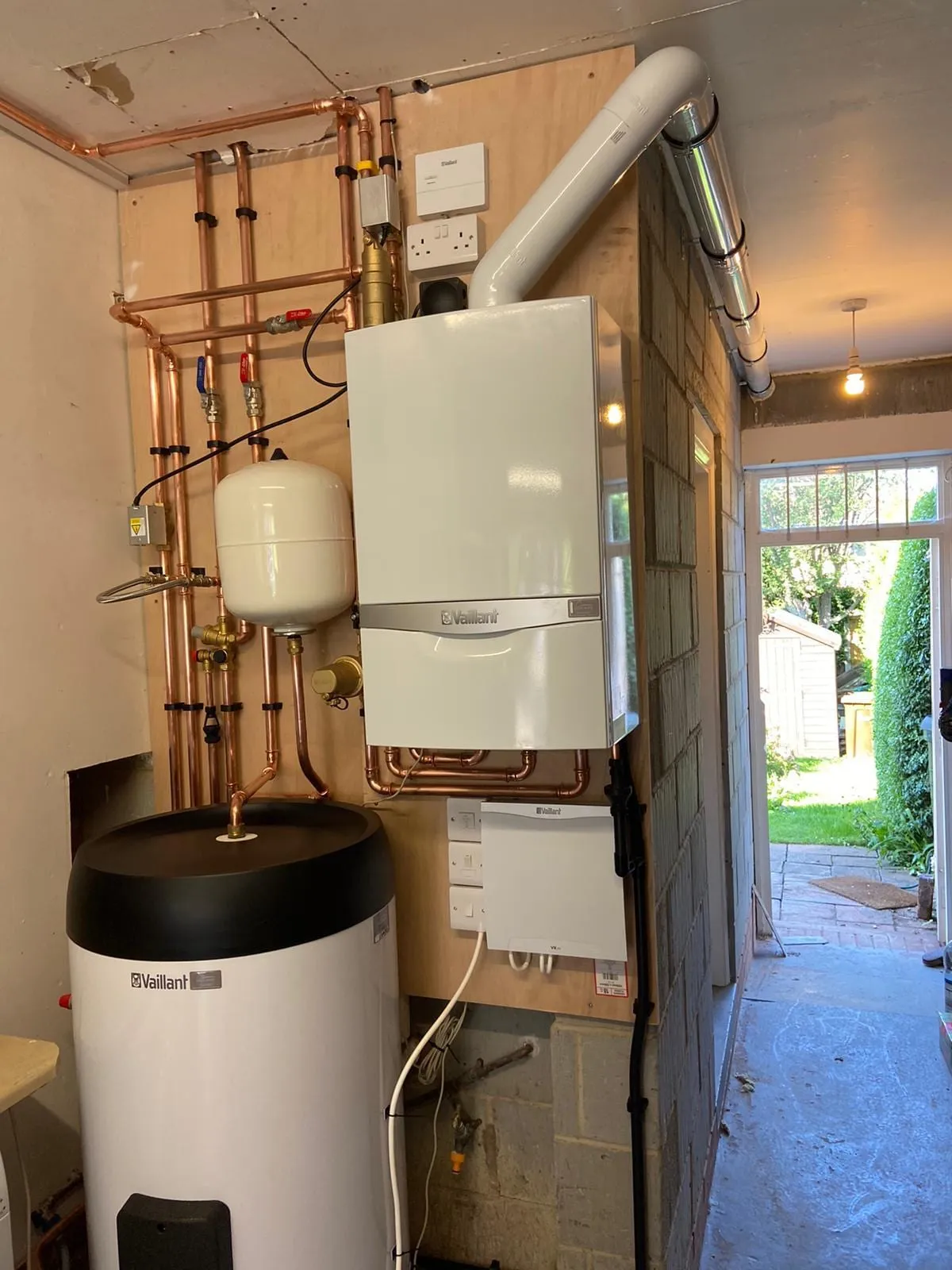 A boiler and cylinder installed beside a doorway, with the copper pipework run up the wall