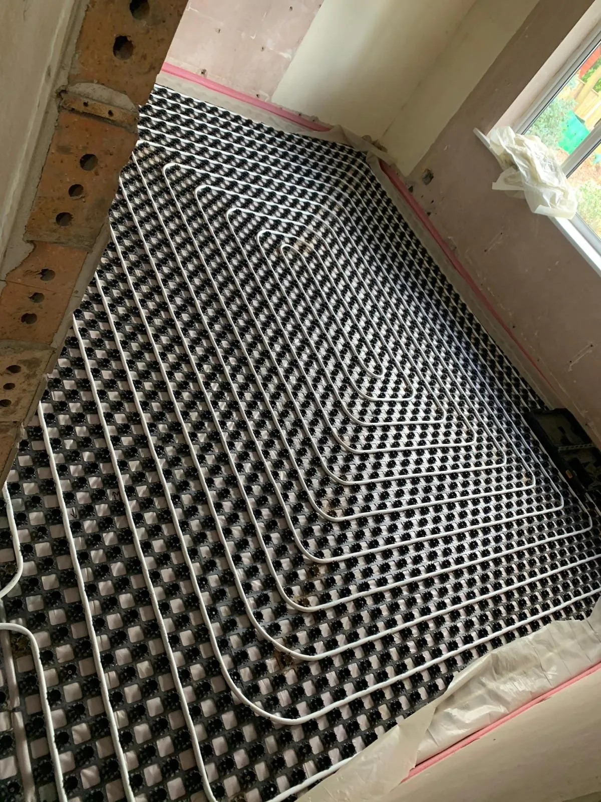 Underfloor heating pipe clipped into a castellated mat across a room before screeding