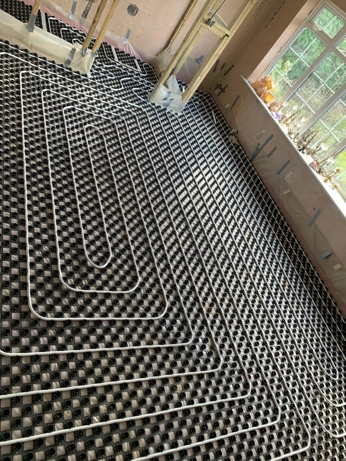 A run of underfloor heating pipe turning back on itself across a castellated mat