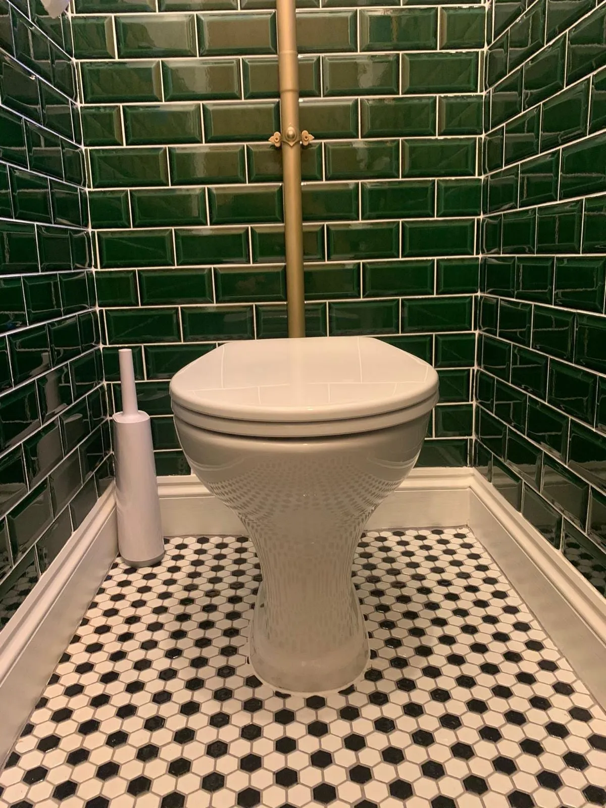 A cloakroom toilet against dark green metro tiling with a black and white patterned floor